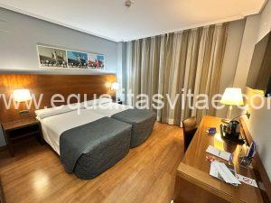 Imagen del interior de la habitación con dos camas juntas, a los pies hay un escritorio.