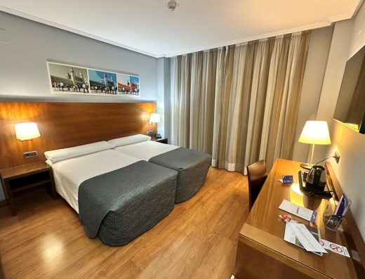 Imagen del interior de la habitación con dos camas juntas, a los pies hay un escritorio.