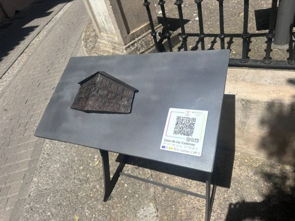 Imagen de una mesa con la escultura en relieve de la fachada de la casa. Incluye código QR.