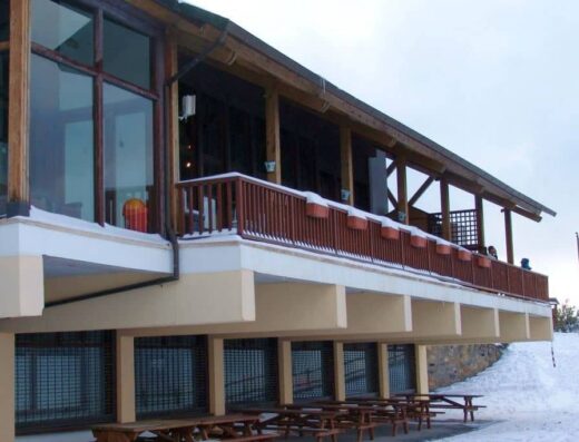 Imagen invernal con nieve. Zona exterior con mesas con bancos de amdera.
