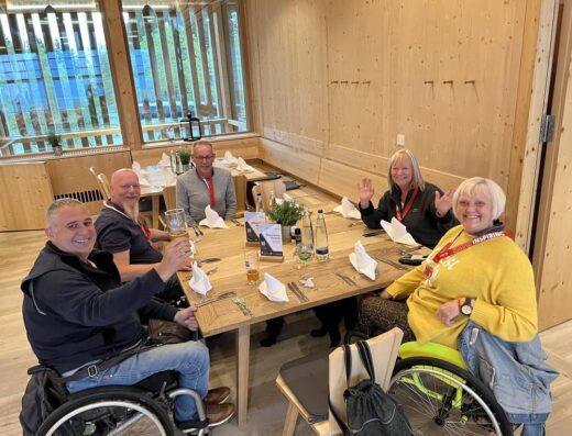 Grupo de personas disfrutando de una comida, dos de ellos son usuarios de silla de ruedas.