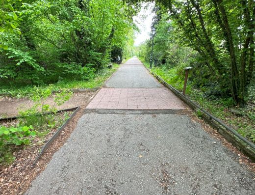 Imagen de tramo de sendero con pavimento podo táctil junto a panel.