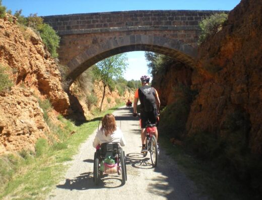Usuario de silla de ruedas y ciclista van a atravesar bajo un puente.