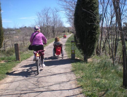 Usuario de silla de ruedas y ciclista recorren la vía.