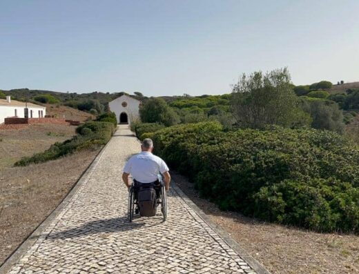 Usuario de silla de ruedas recorre el camino hacia la ermita que se sitúa al fondo.