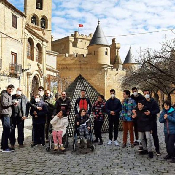 Grupo de personas con discapacidad, dos de ellas en silla de ruedas con el castillo al fondo.