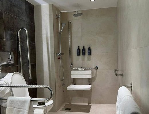 Inodoro con barras de apoyo y ducha a cota cero con silla de ducha.