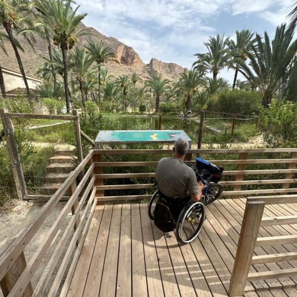 Imagen de usuario de silla de ruedas junto a mirador de una pequeña laguna.