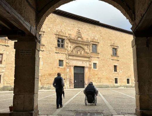 Imagen de usuario de silla de ruedas junto acompañante en el casco histórico de la localidad.