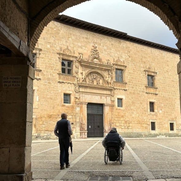 Imagen de usuario de silla de ruedas junto acompañante en el casco histórico de la localidad.