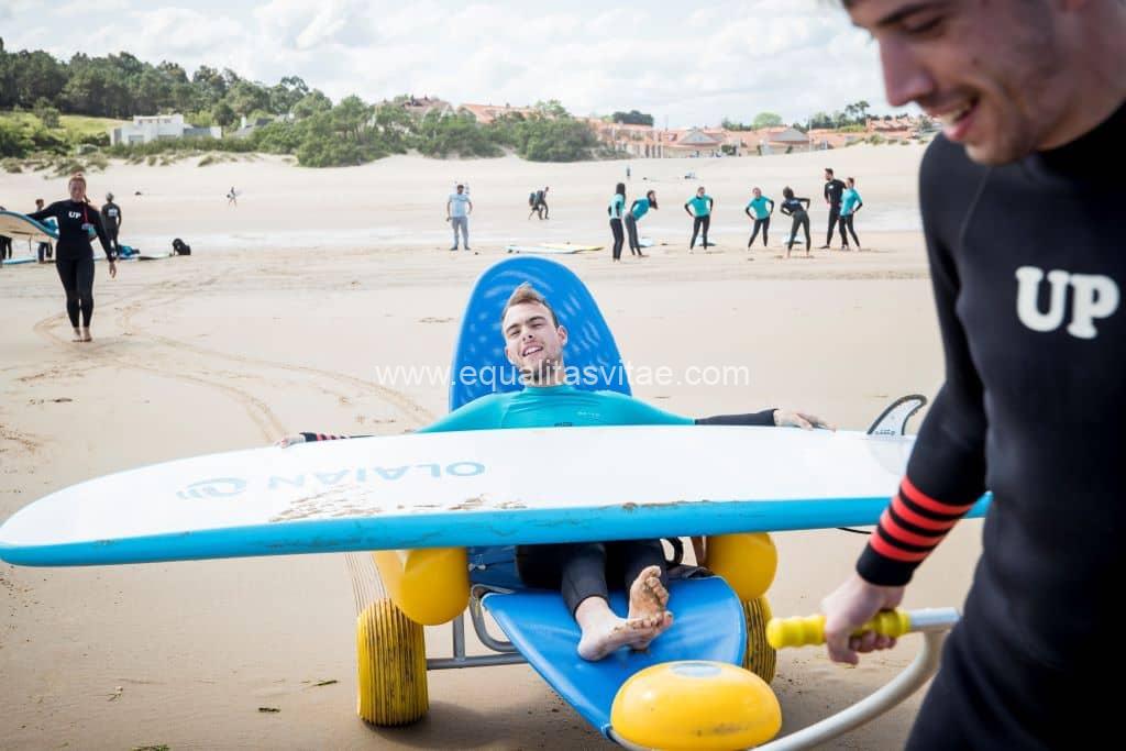 Imagen de persona con discapacidad en una silla anfibia con una tabla de surf sobre sus piernas.