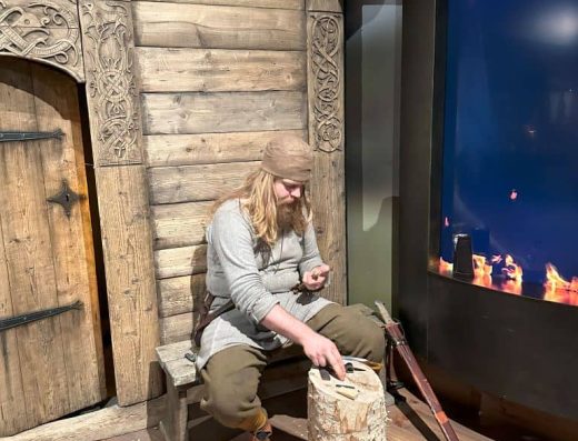 Imagen de vikingo trabajando junto a la entrada de una casa.