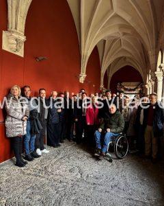 Imagen de un grupo de personas, uno de ellos en silla de ruedas bajo un pórtico de arcos apuntados.