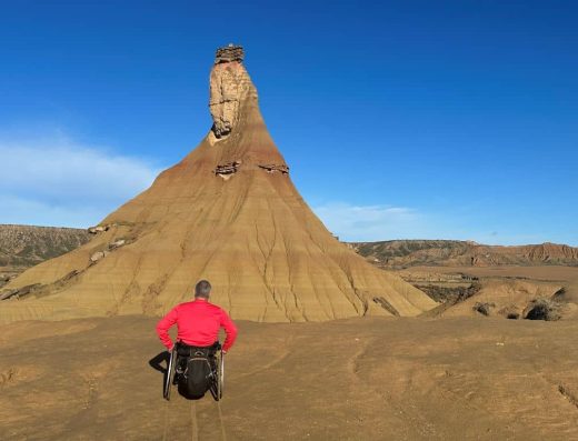 Imagen de usuario de silla de ruedas frente al monumento natural de castildetierra.