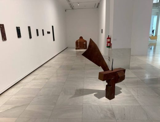 Imagen de una sala diáfana con exposición pictórica en sus paredes y alguna escultura de arte contemporáneo.