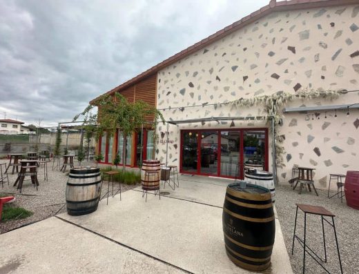 Imagen del acceso al interior del restaurante con barricas como mesas taburetes altos.