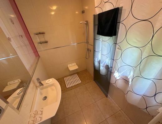 Imagen del interior del baño, zona de la ducha, a cota cero, con mampara abatible y asiento.