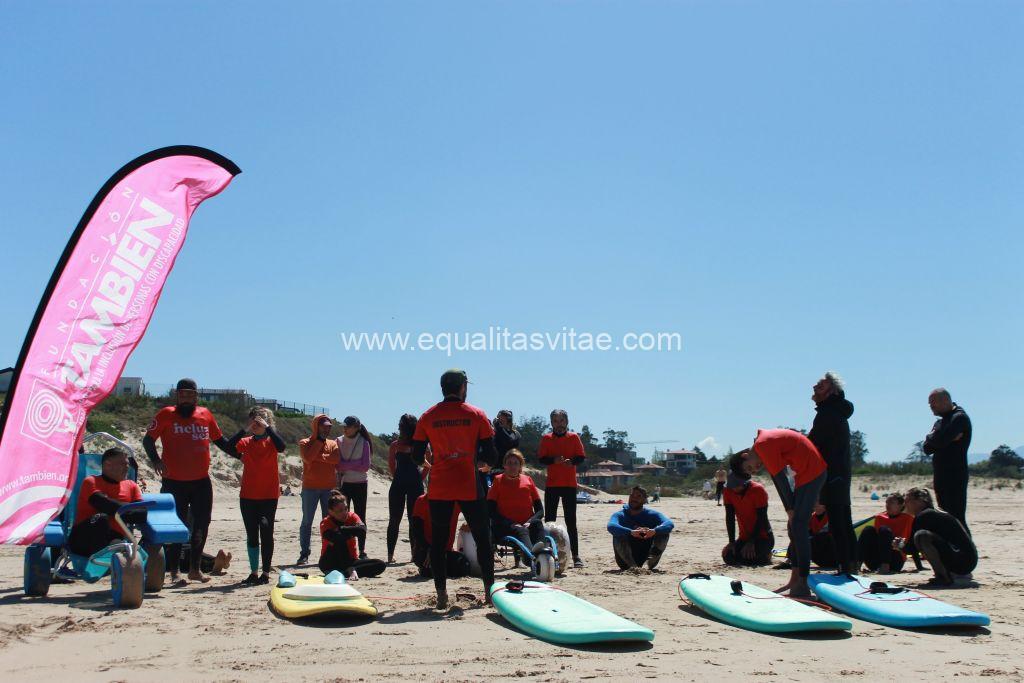 Imagen de un grupo de personas con los monitores junto a unas tablas de surf. Algunos de los participantes van en silla de ruedas.