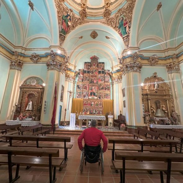 Imagen de persona usuaria de silla de ruedas en el interior de la iglesia acercándose al retablo mayor.