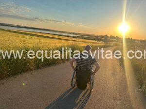 Imagen de una persona en silla de silla de ruedas recorriendo un sendero junto a la laguna al atardecer.
