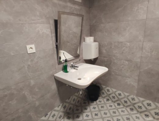 Imagen del lavabo, sin pie, con grifo monomando largo y espejo inclinado.
