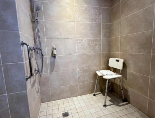 Imagen de la ducha a cota cero con silla y barras de apoyo.