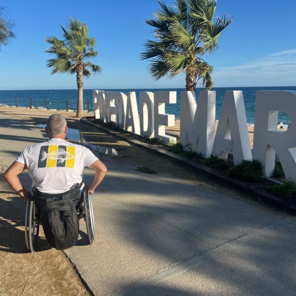 Imagen de una persona en silla de ruedas por el paseo marítimo junto a las letronas de Pineda de Mar.