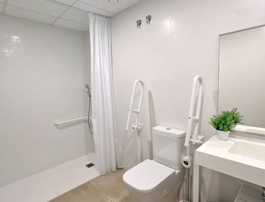 Imagen del interior del baño con inodoro con barras de apoyo y ducha a cota cero.