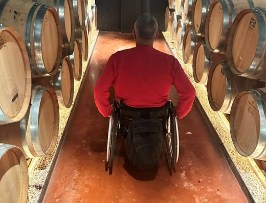 Imagen de una persona en silla de ruedas recorriendo la nave de barricas.