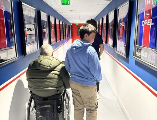 Imagen de varias personas recorriendo un pasillo del museo., una de ellas en silla de ruedas. En las paredes distintos cuadros con camisetas del PSG.