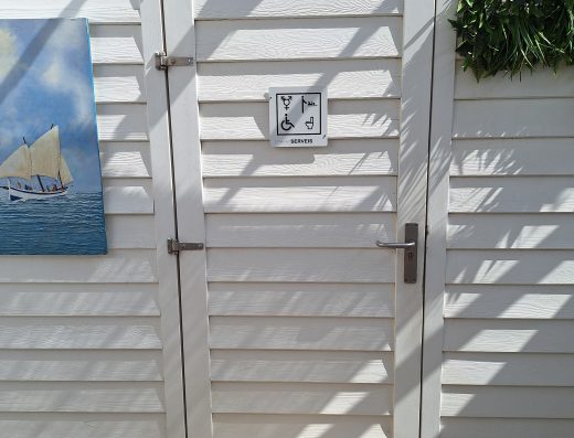 Imagen de la puerta de entrada a un aseo, señalizada con pictogramas: símbolo masculino y femenino, inodoro, cambiador de bebé y silla de ruedas.