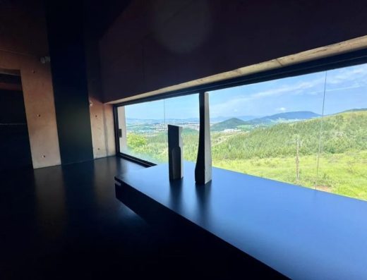 Imagen de una de las salas con dos esculturas con forma de prisma junto a un ventanal desde el que se observa el paisaje montañoso verde.