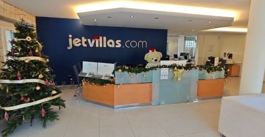 Imagen de un mostrador de recepción con el nombre de la empresa en la pared que hay justo detrás. El nombre de la empresa en jetvillas.com.