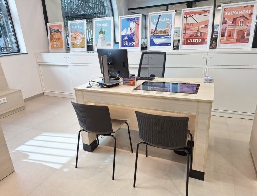 Imagen de una mesa de oficina para atender al público con dos mesas de confidente. Cuenta con un ordenador de sobremesa.