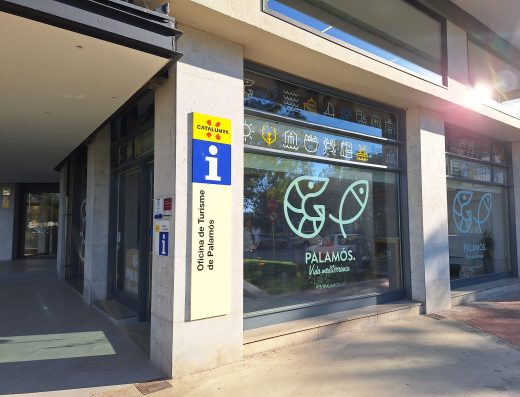Imagen de la fachada de la oficina de turismo de Palamós con ventanales con pictogramas referente al turismo de Palamós. Pictogramas de pescados, barco, sol, olas del mar.