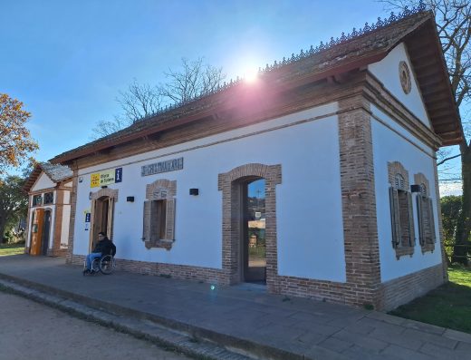Imagen panorámica del edificio en el que se ubica la oficina, de una sola planta con techo a dos aguas. En la acera, junto a la puerta de entrada hay una persona en silla de ruedas.