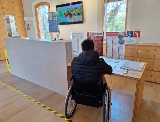 Imagen de una persona en silla de ruedas en el mostrador adaptado de una recepción.