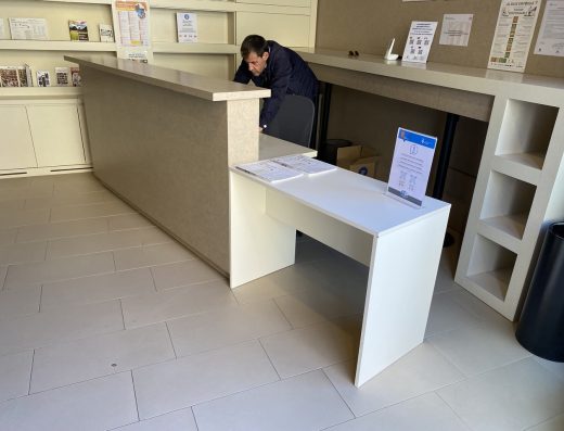 Imagen del mostrador de una oficina de turismo. Mostrador a doble altura. Un hombre está junto a la silla que hay en el mostrador de altura estándar.