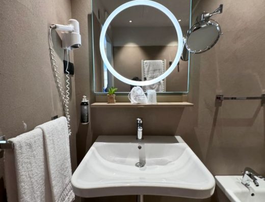 Imagen de la zona del lavabo, sin pie, grifo monomando y espejo con un aro de luz en el interior.