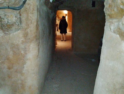 Imagen del interior de la bodega con paredes de piedra. Al fondo de una pasillo se observa la figura de una mujer.