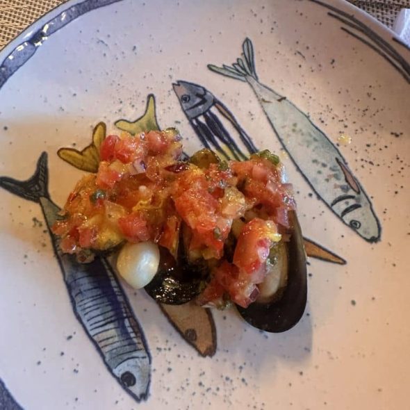 Imagen de un pincho de mejillón sobre un plato decorado con varios pescaditos.