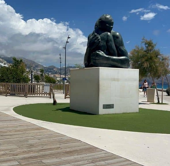Imagen de un paseo con una gran figura sobre un pedestal que representa un abrazo.