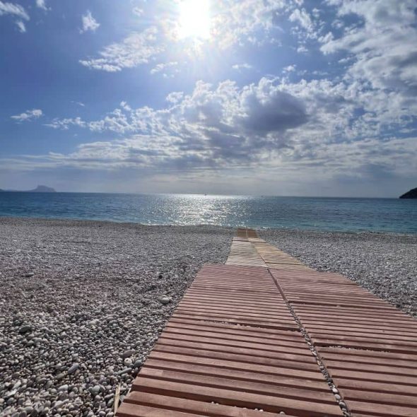 Imagen de la tarima que lleva al mar en una playa de piedra de canto rodado.