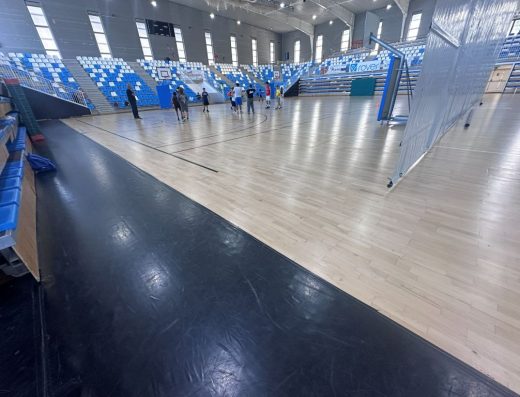 Imagen de una cancha de un pabellón deportivo con un grupo de personas en la parte central escuchando al entrenador.