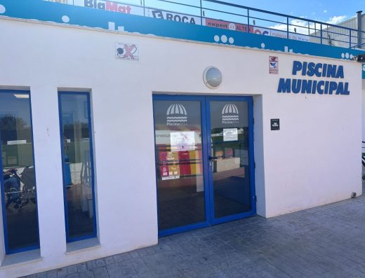 Imagen de la entrada al edifico que alberga la Piscina Municipal de Altea, señalizado junto a la entrada.