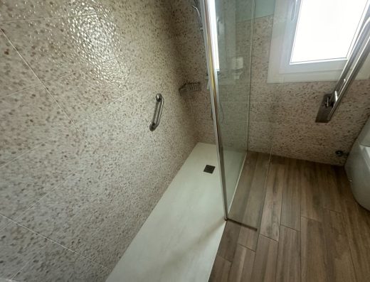 Imagen de una ducha a cota cero con mampara en el lateral.