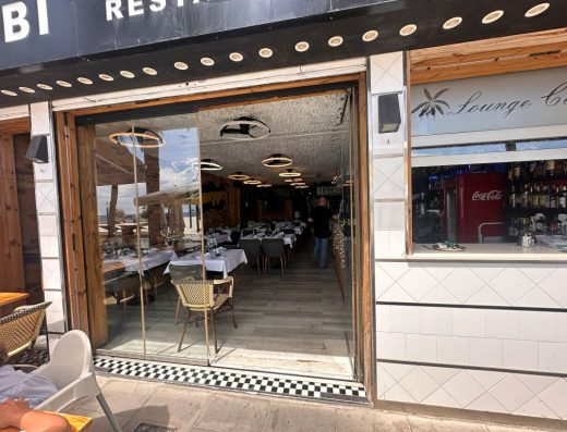Imagen de la entrada al restaurante a través de puerta acristalada. a la derecha de la entrada hay una ventana para atender a los clientes.