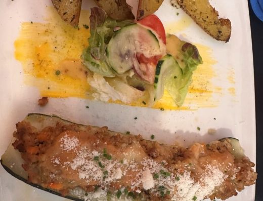 Imagen de un plato con un calabacín relleno de carne acompañado por una pequeña ensalada y patatas panadera.