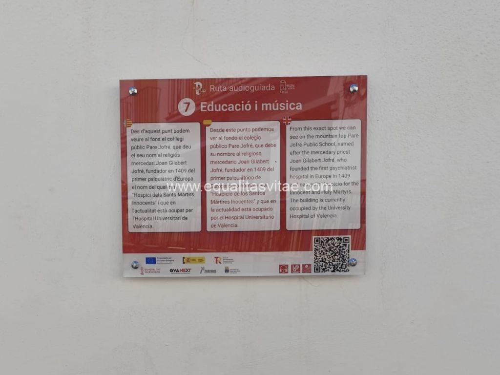 Imagen de una placa informativa de la ruta de El Puig con el título el Educació i música, el contenido está en valenciano, español e inglés. Abajo en la derecha se encuentra el código QR que enlaza al contenido digital accesible.