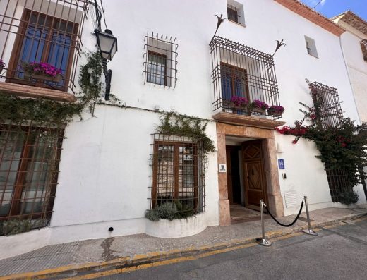 Imagen de la fachada principal del alojamiento. Fachada blanca con balcones enrejados y decorados con macetas.